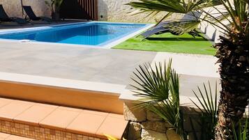 Una piscina con un muro de piedra, césped y una palmera.
