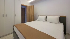 A bedroom with a bed, a wardrobe, and a door leading to another room. - Alexandros Two-Bedroom Deluxe Suite n. 11 (Paralia)