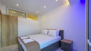 A modern bedroom with a bed, bedside table, and a wardrobe. - Alexandros Two-Bedroom Deluxe Suite n. 11 (Paralia)