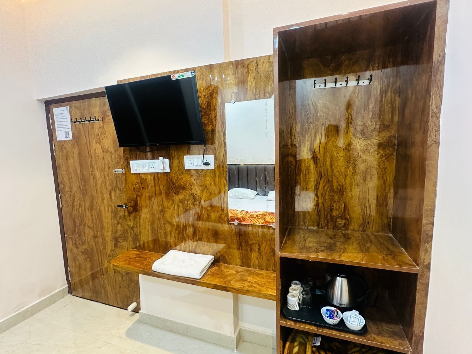 Une salle de bain avec un meuble-lavabo en bois, un miroir, un téléviseur fixé au mur et une étagère contenant des articles de toilette.