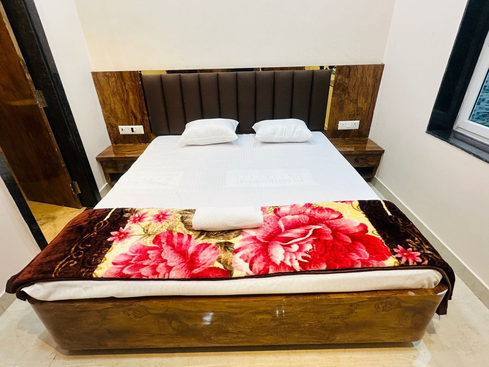 Un lit bien fait, avec une couette à motifs floraux, une tête de lit en bois et des tables de chevet dotées de lampes.
