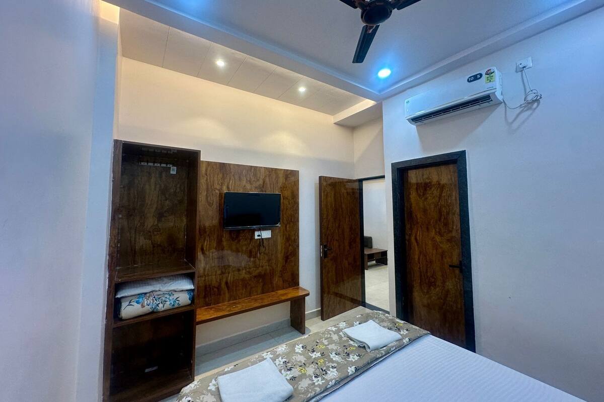A hotel room with a bed, a TV mounted on the wall, a ceiling fan, and an air conditioning unit.