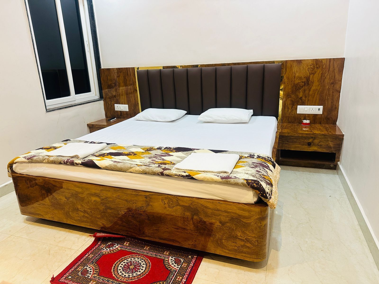 A bed with a wooden headboard, a bedside table, and a red patterned rug.