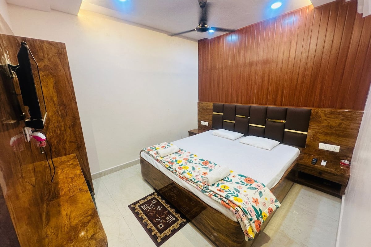 A bedroom with a wooden headboard, a bed with floral bedding, a ceiling fan, and a nightstand with a remote control.