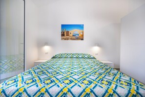 A bedroom with a bed, a painting of a coastal scene, and two bedside lamps. - O Molu Apartment (Sicilia)