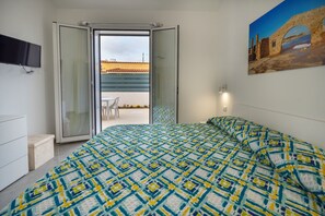 A bedroom with a bed, a TV, a sliding glass door leading to an outdoor area, and a painting on the wall. - O Molu Apartment (Sicilia)