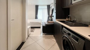 A compact hotel room with a kitchenette, a washing machine, and a bed with a view of the city. - Embassy Gardens (Accra)