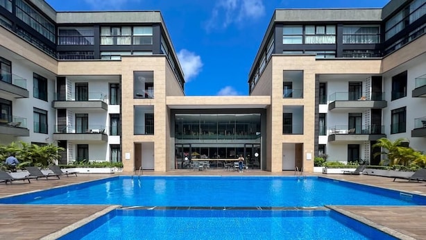 A modern hotel with a central pool, multiple balconies, and a clear sky. - Embassy Gardens (Accra)