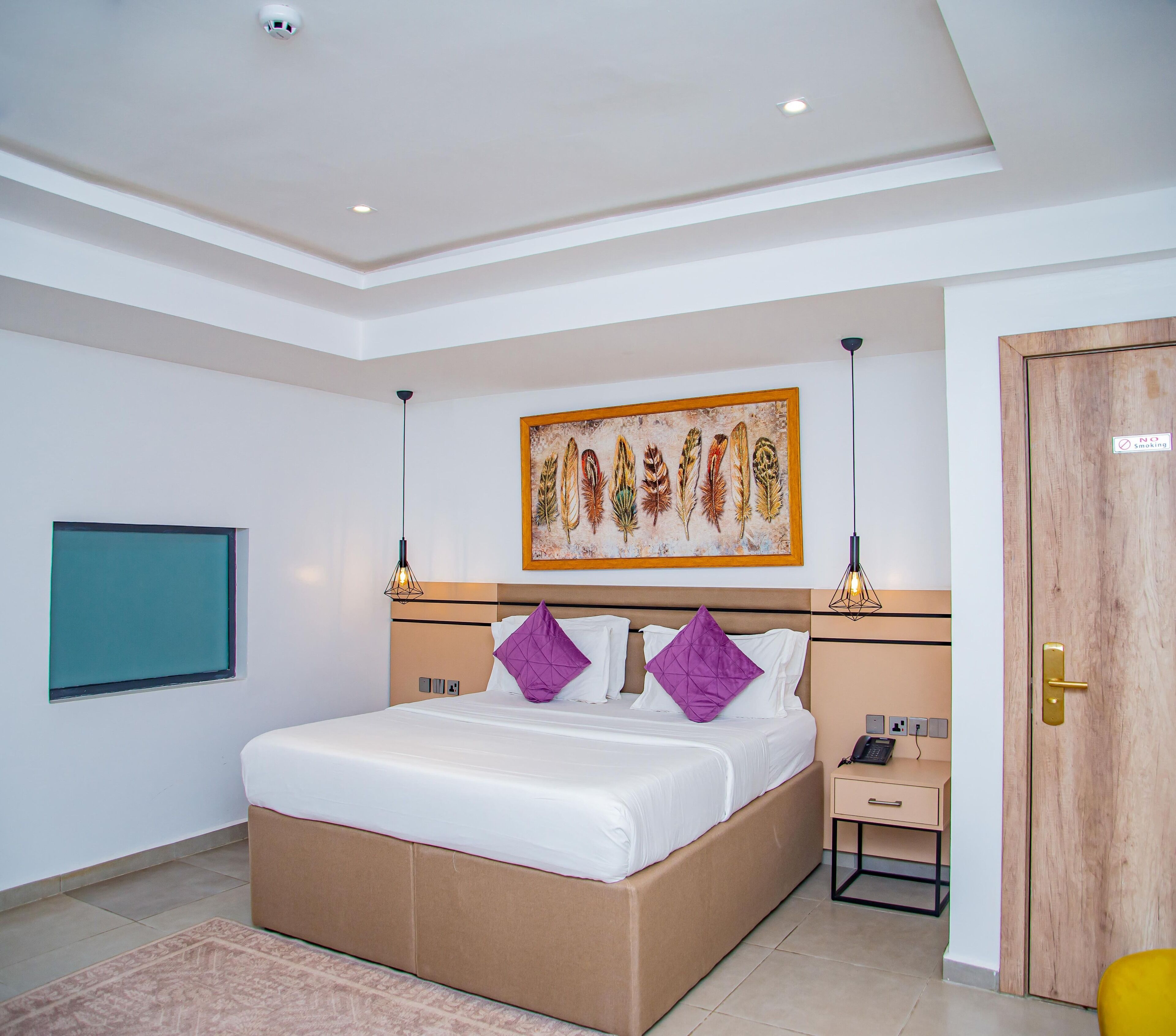 Une chambre d’hôtel moderne avec un grand lit, une table de chevet, un bureau, une porte en bois et un tableau au mur.