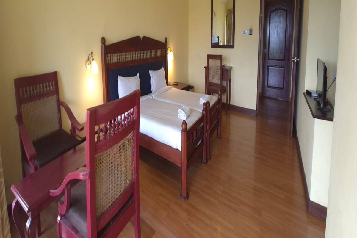 A hotel room with a wooden bed, two chairs, a small table, a mirror, and a door.