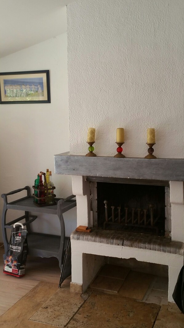 Ein Kamin mit drei Kerzen, ein gerahmtes Bild an der Wand und eine Tüte mit Grillzubehör auf dem Boden.