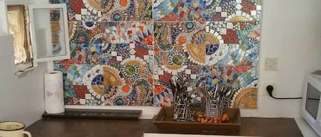 Una cocina compacta con salpicadero de azulejos, un lavamanos, un microondas y un cubo rojo.