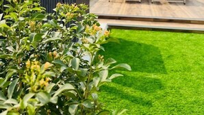 Terraza en la azotea con piso de madera, un banco blanco y plantas en macetas.