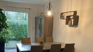 Un espace repas comprenant une table et des chaises, un luminaire suspendu et une vue sur la verdure à l’extérieur.