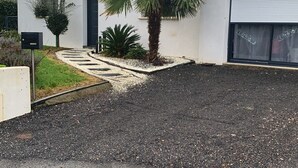 Un bâtiment moderne à l’extérieur blanc, doté d’une porte de garage et d’une allée gravillonnée.