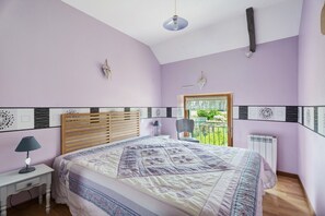 A bedroom with a bed, bedside table, lamp, and a window with a view. - Holiday Home "Gîte Les Hortensias with Pool" – Private Pool, Wi-Fi & Air Conditioning (Trébédan)