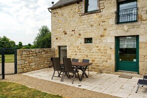 A stone building with a green door, a small window, and a patio with a table and chairs. - Holiday Home "Gîte Les Hortensias with Pool" – Private Pool, Wi-Fi & Air Conditioning (Trébédan)