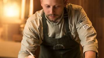 A person in a chef's uniform preparing food at a counter with a plate of food and a bowl of ingredients.