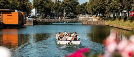 Een boot met passagiers op een gracht, omringd door bomen en gebouwen.