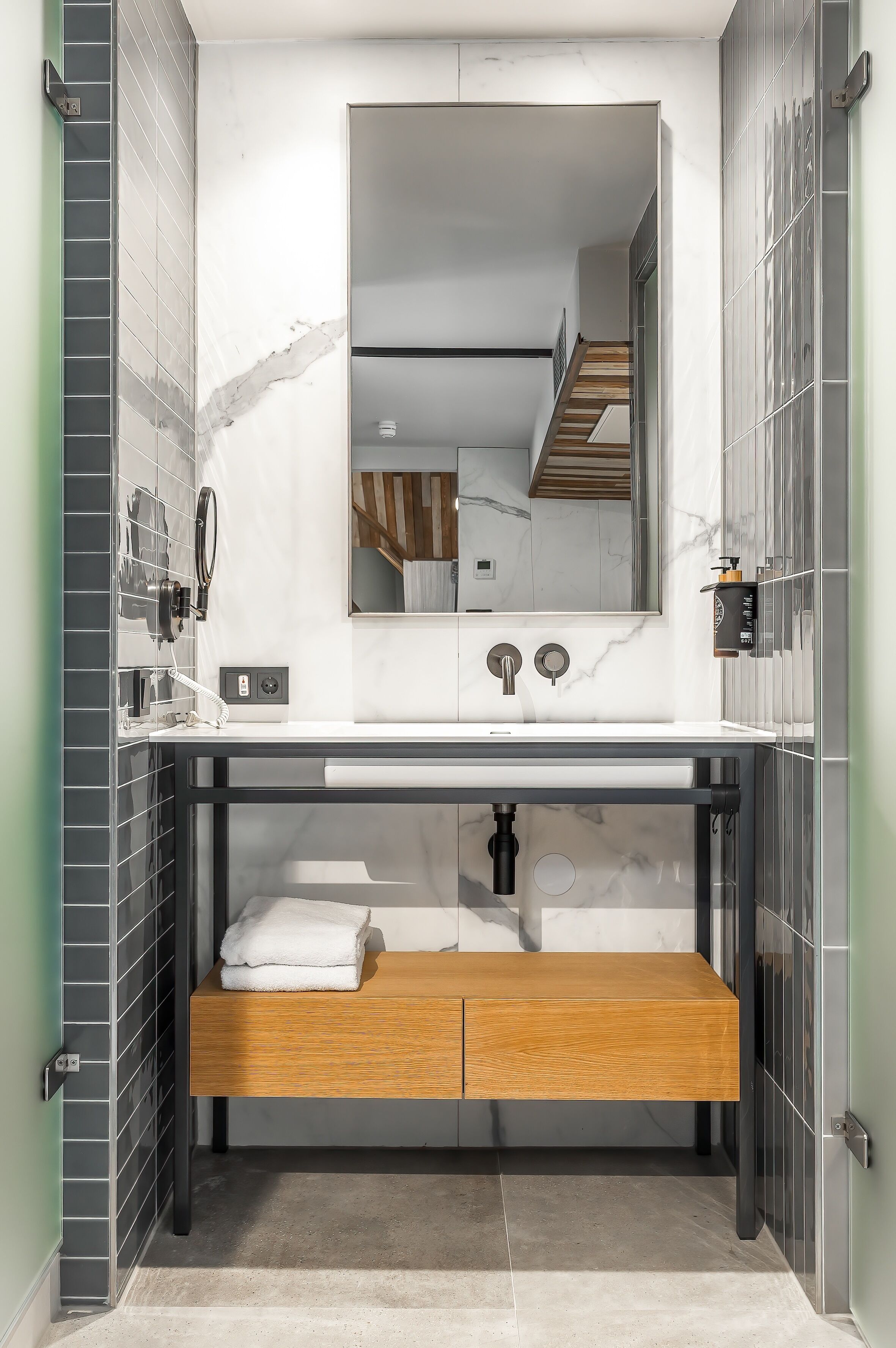 A modern bathroom with a marble vanity, a wooden bench, and a large mirror.