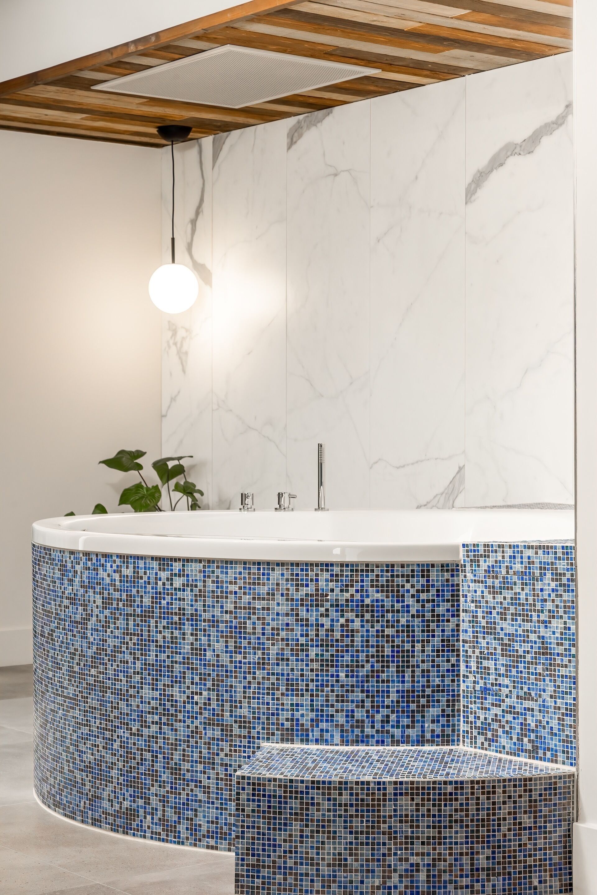 A bathroom with a marble wall, a blue mosaic tub, and a wooden ceiling.