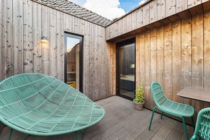 Un terrazzo in legno con due sedie verdi e un tavolo, una porta che dà su una stanza e una pianta in vaso.