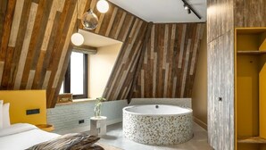 Un dormitorio moderno con techo inclinado, una bañera redonda y una cama con cabecero de madera.