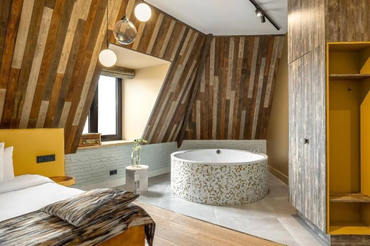 A modern bedroom with a sloped ceiling, a round bathtub, and a bed with a wooden headboard.