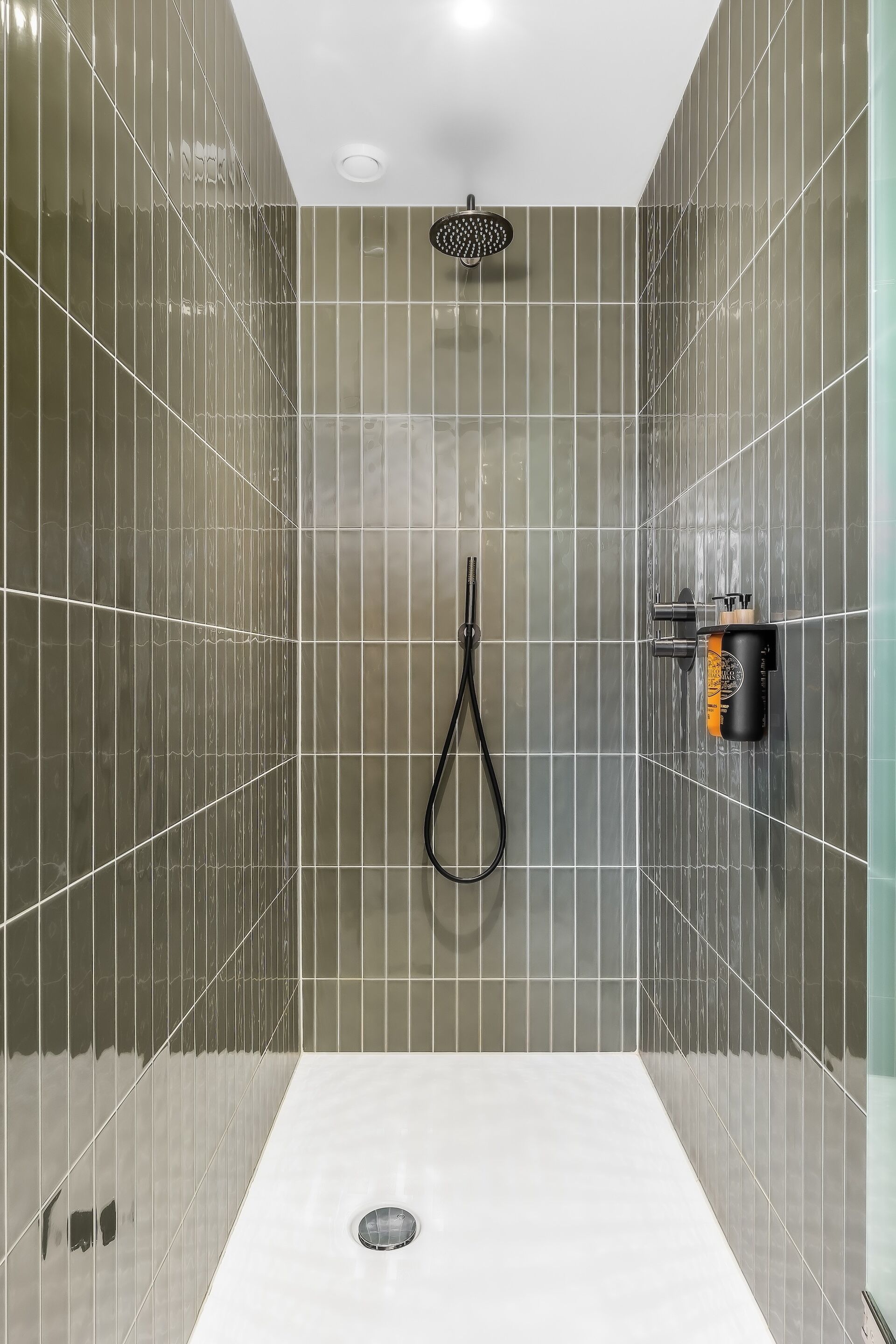 Un baño moderno con ducha, cabezal de ducha de mano y calentador de agua instalado en la pared.