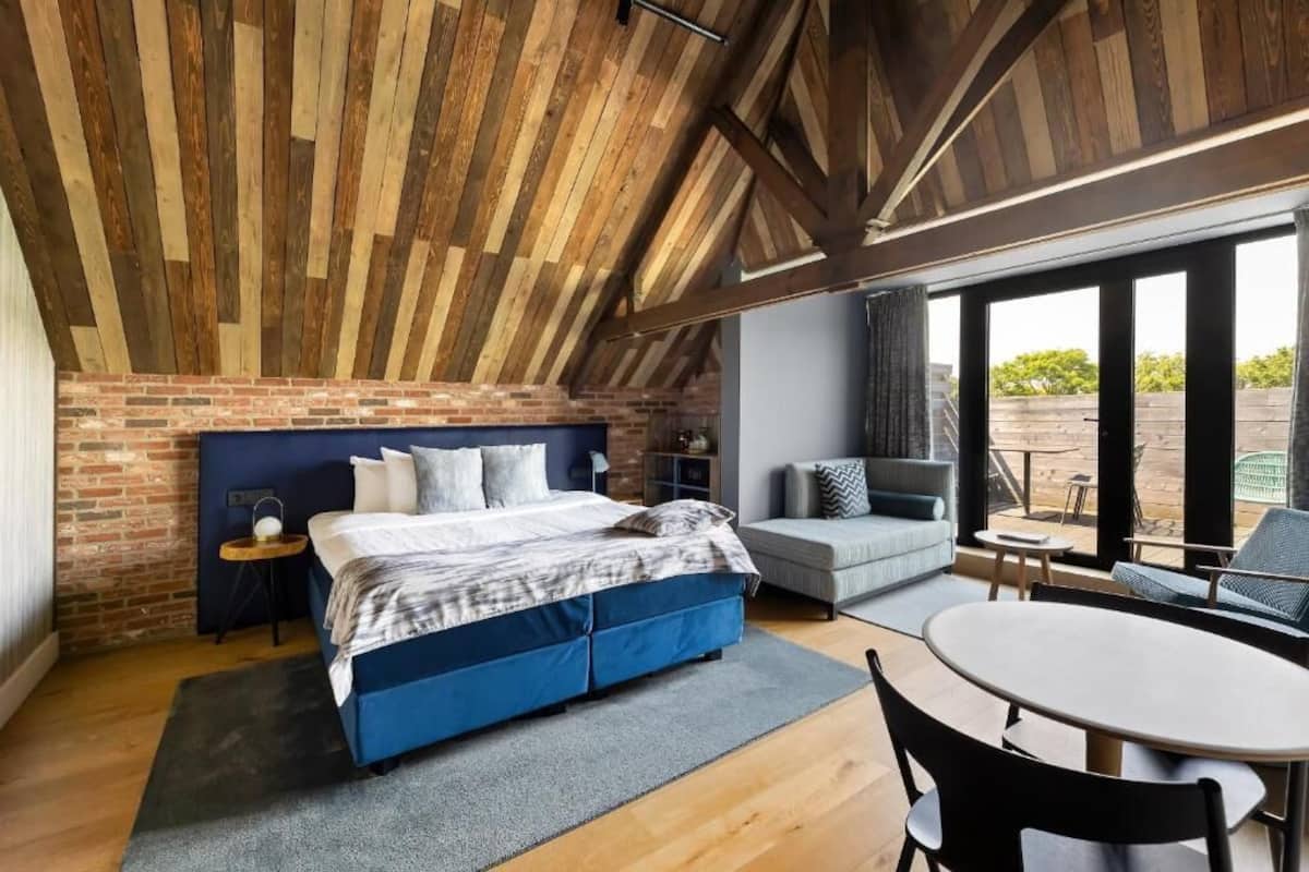 A bedroom with a brick wall, a bed, a small table, and a sofa.