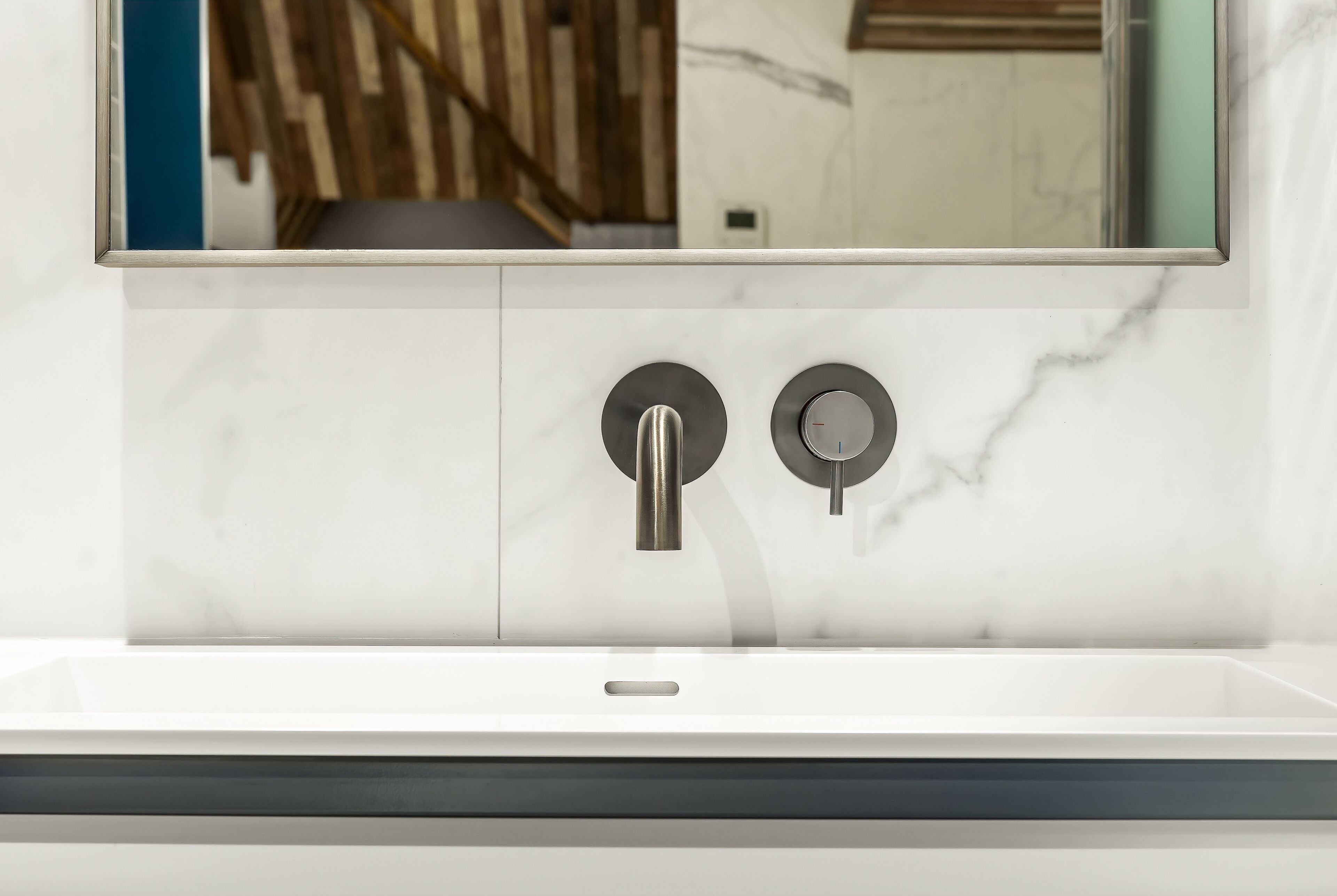 A modern bathroom with a white marble sink, two round faucets, and a large mirror above.