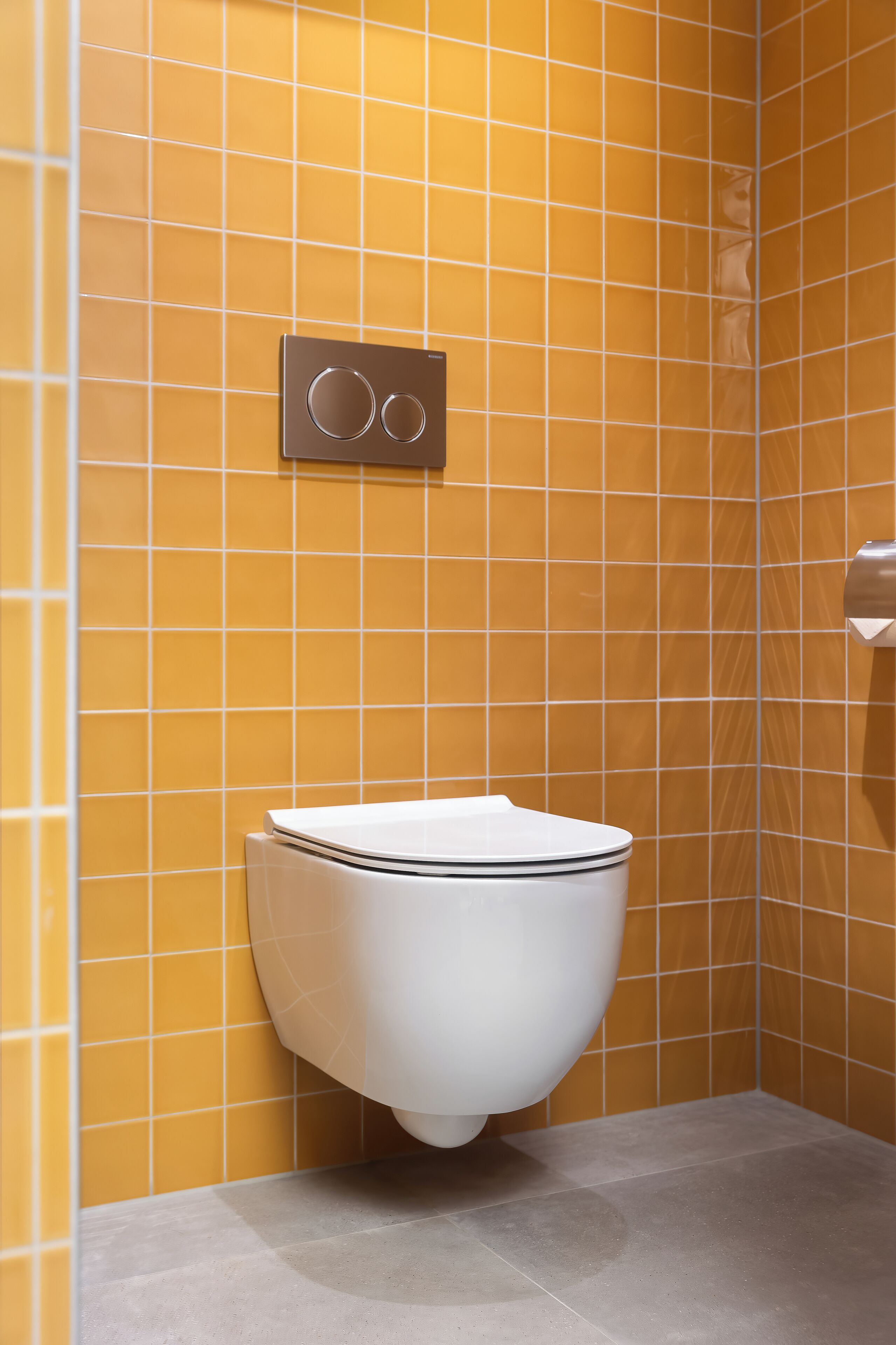 A toilet in a bathroom with yellow tiled walls and a grey floor.