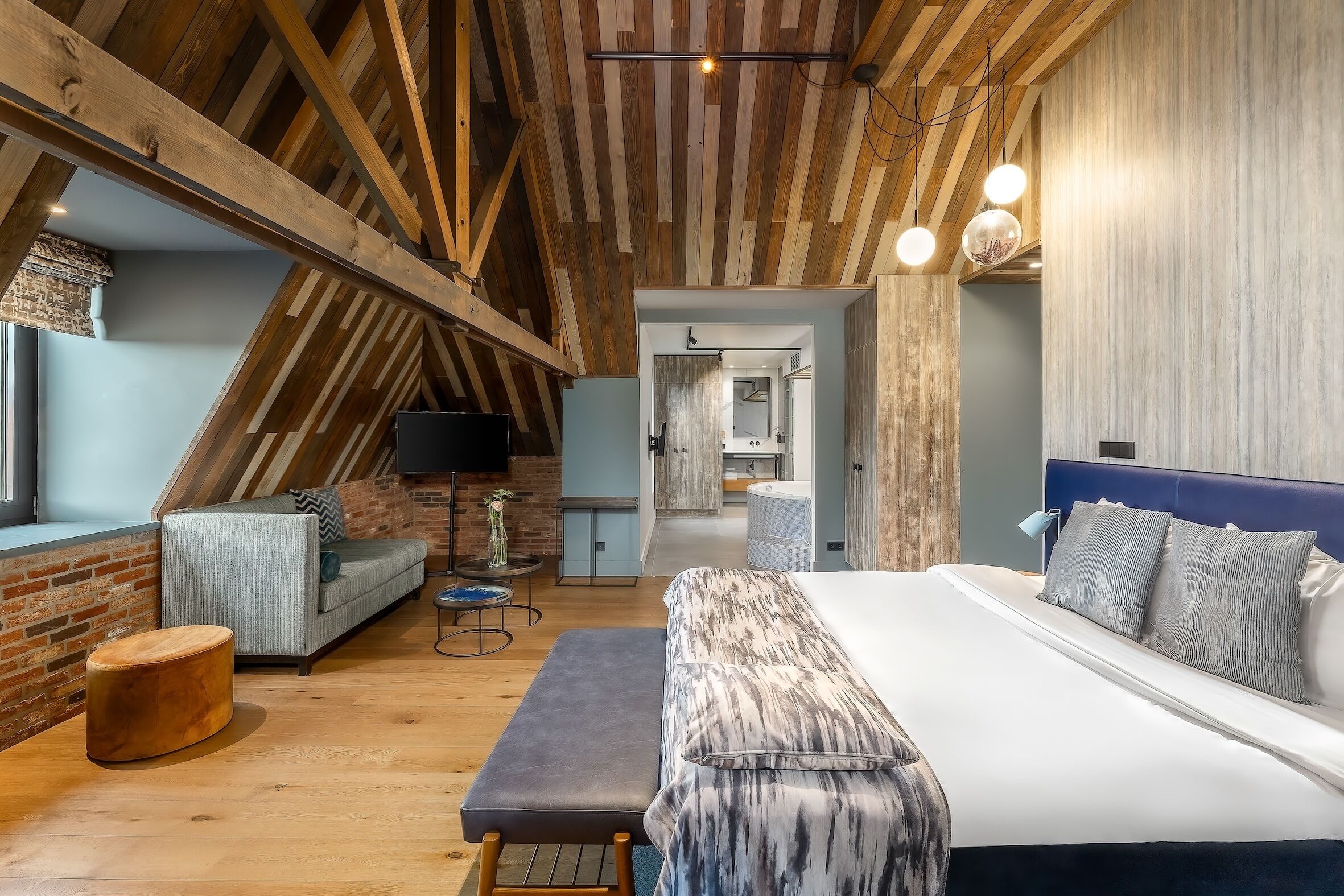 Een moderne slaapkamer met een groot bed, een bank, een houten bankje en een televisie.