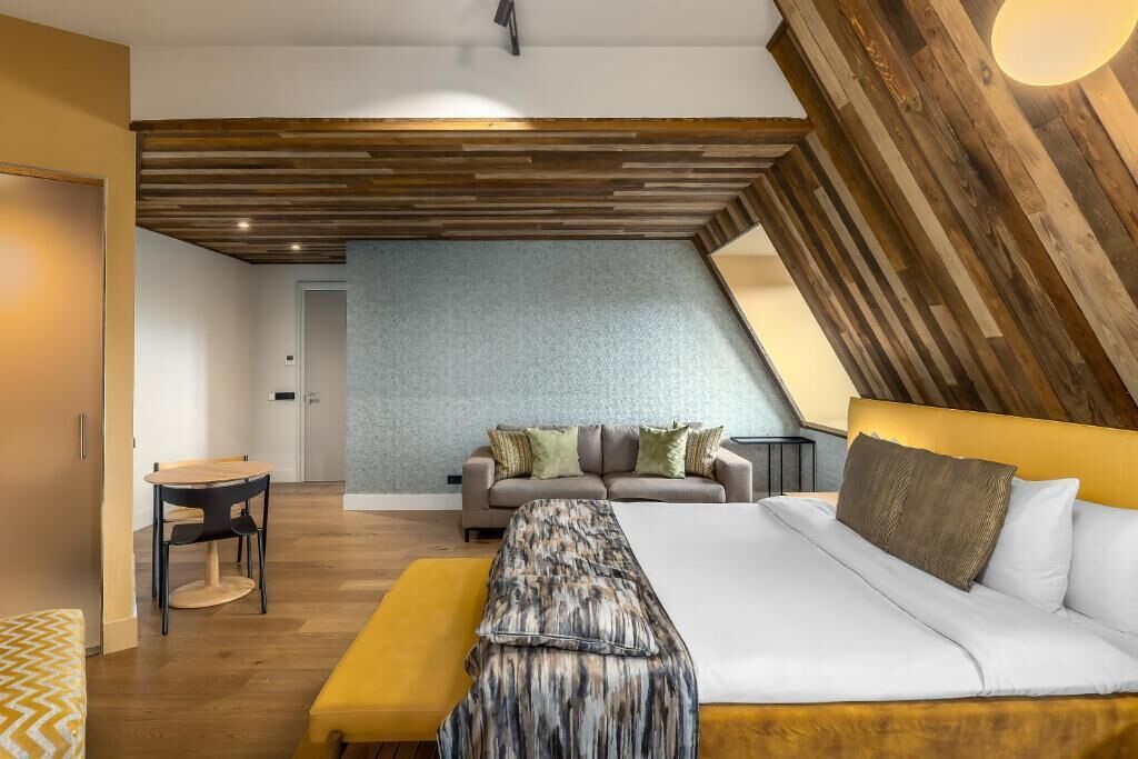A modern bedroom with a sloped ceiling, a bed, a sofa, and a small table.
