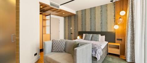 Una habitación de hotel moderna con una cama, un sofá, una mesita y un vestidor.