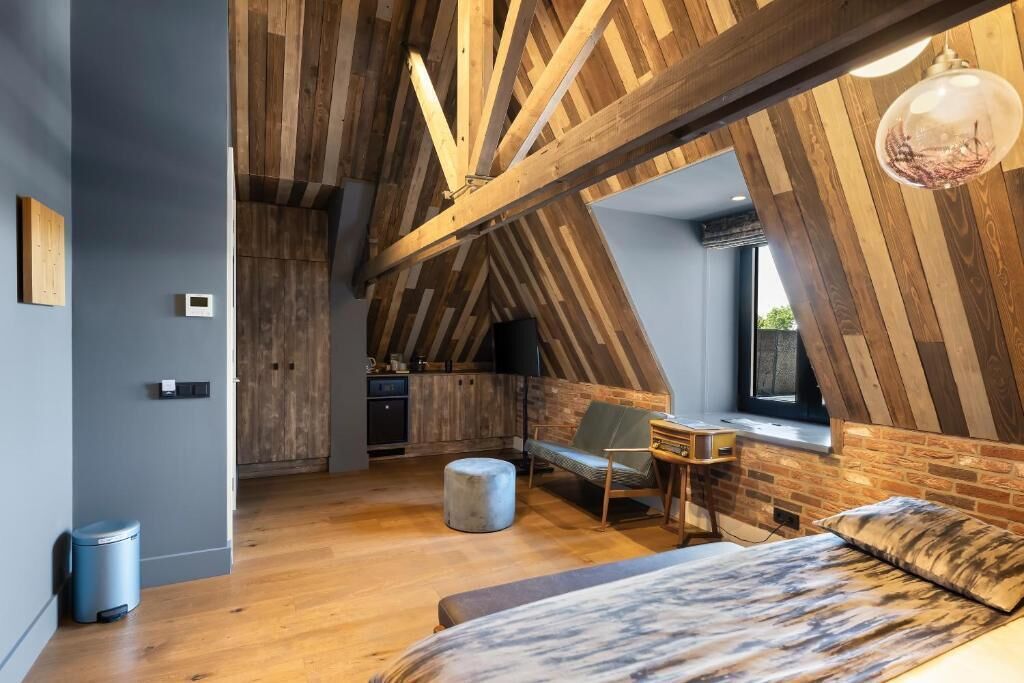 Une chambre à coucher aménagée dans un espace de type « loft », avec des poutres apparentes, un lit, un bureau et une fenêtre.