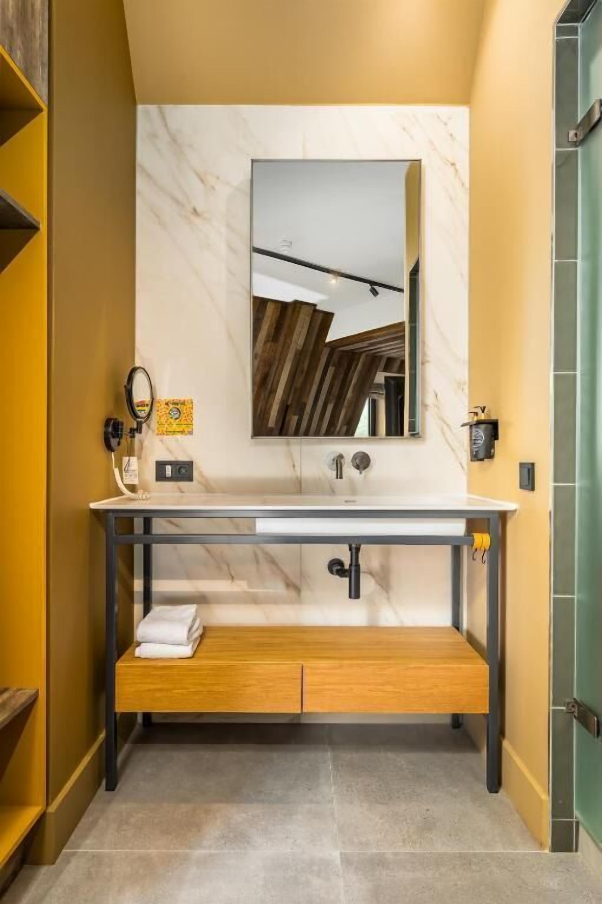 Een moderne badkamer met een marmeren wastafel, een houten bankje en een grote spiegel.
