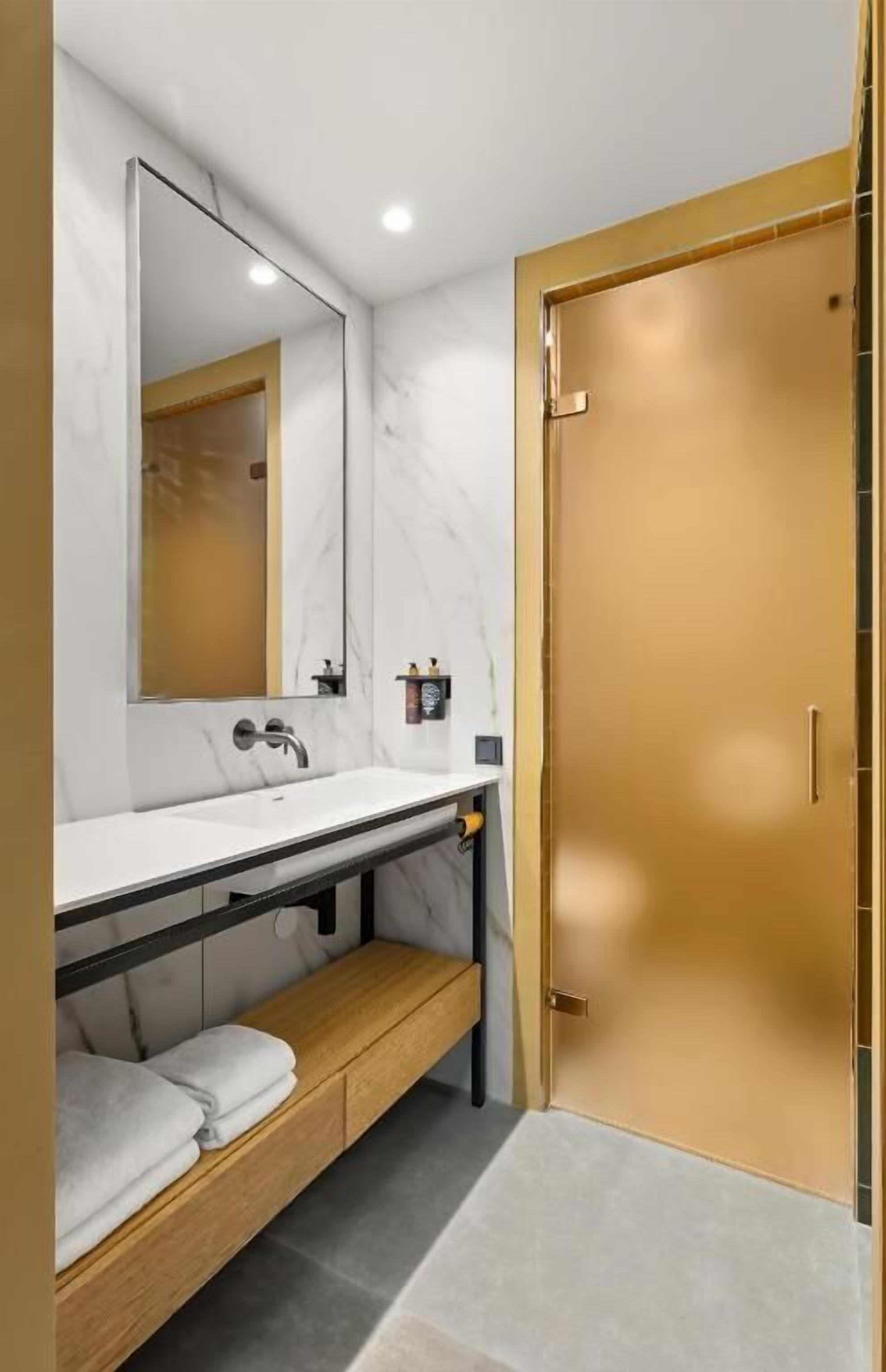 Un baño moderno con un lavabo de mármol blanco, un espejo grande y un banco de madera.