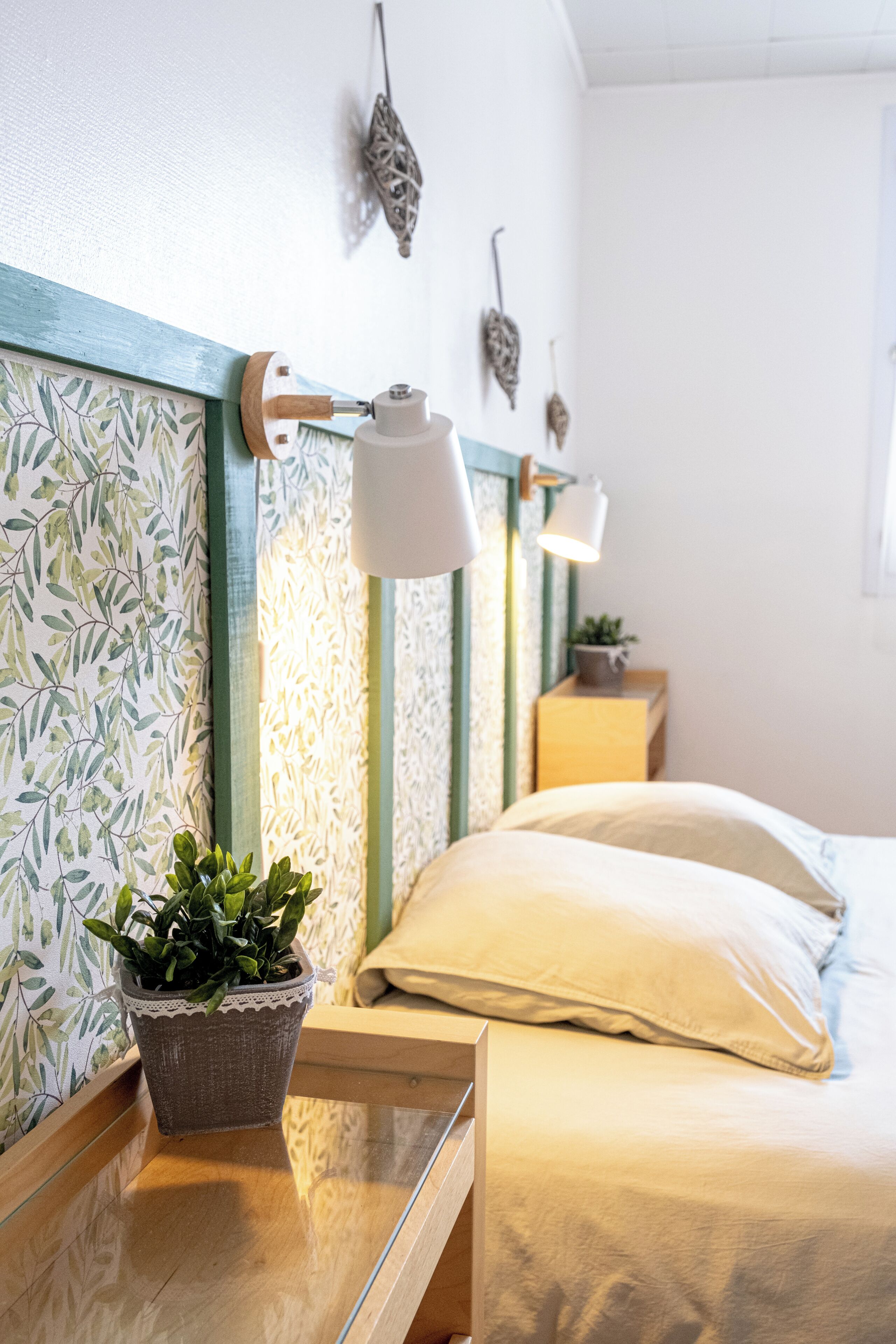 Une chambre à coucher bien rangée, avec un lit, des tables de chevet, une plante en pot et des lampes fixées au mur.
