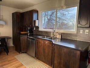 Eine moderne Küche mit dunklen Holzschränken, einem Edelstahl-Geschirrspüler, einer Spüle und einem Fenster mit Blick auf Bäume.