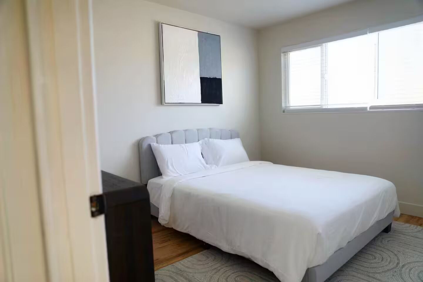 Quarto com cama, mesa de cabeceira, janela e um quadro na parede.