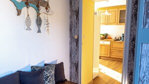 A wooden bench with cushions, a wall-mounted fish decoration, and a doorway leading to a kitchen with wooden cabinets.