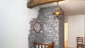 A staircase with a wooden handrail leading to a room with a stone wall and a hanging light fixture.