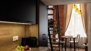 A modern kitchen with a wooden countertop, a coffee machine, and a bowl of fruit. There is a dining area with a table and chairs, and a window with curtains. - L23 Boutique by Downtown Apartments (Kraków)