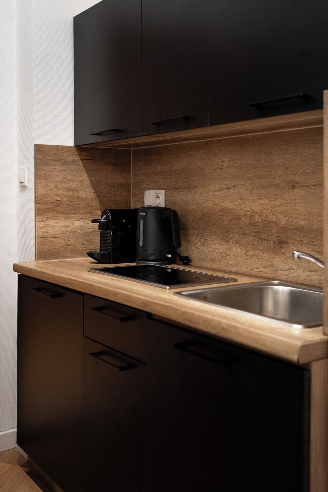 A modern kitchen with a black coffee maker, a stainless steel sink, and wooden cabinetry.