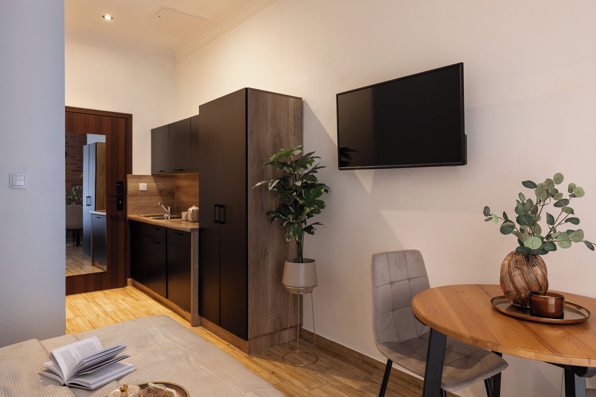 A modern kitchen with dark wood cabinets, a built-in oven, and a flat-screen TV mounted on the wall.