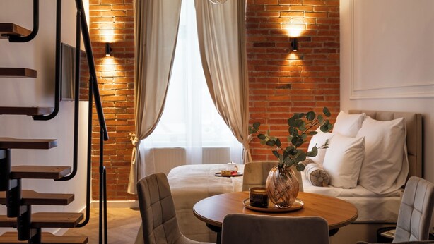 A modern room with a brick wall, a round wooden table, a sofa, and a chair. - L23 Boutique by Downtown Apartments (Kraków)