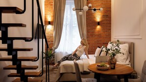 A cozy living room with a brick wall, a sofa, a dining table with a bowl of fruit, and a staircase with wooden steps. - L23 Boutique by Downtown Apartments (Kraków)