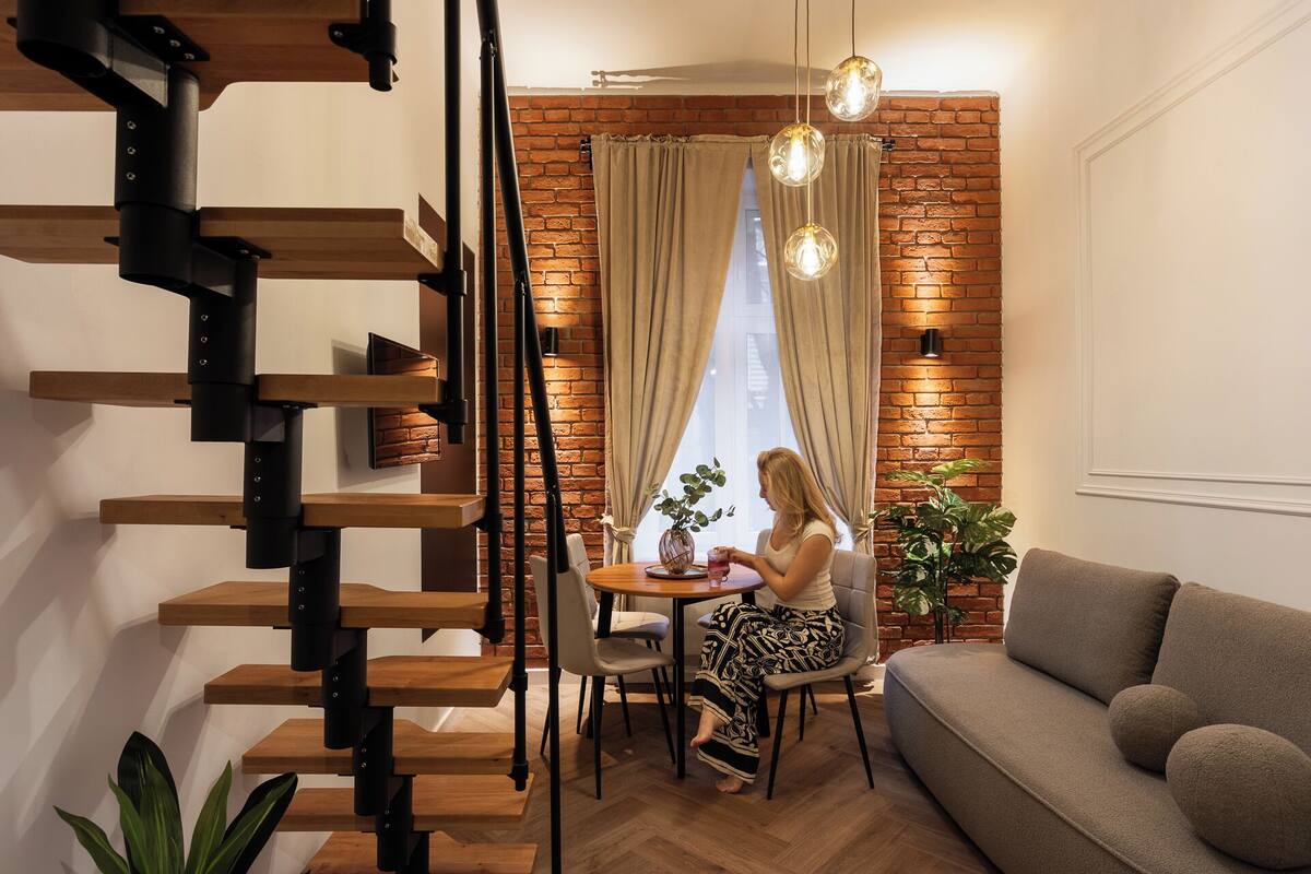 Una sala de estar moderna con una pared de ladrillo, una escalera de madera y un comedor con mesa y sillas.