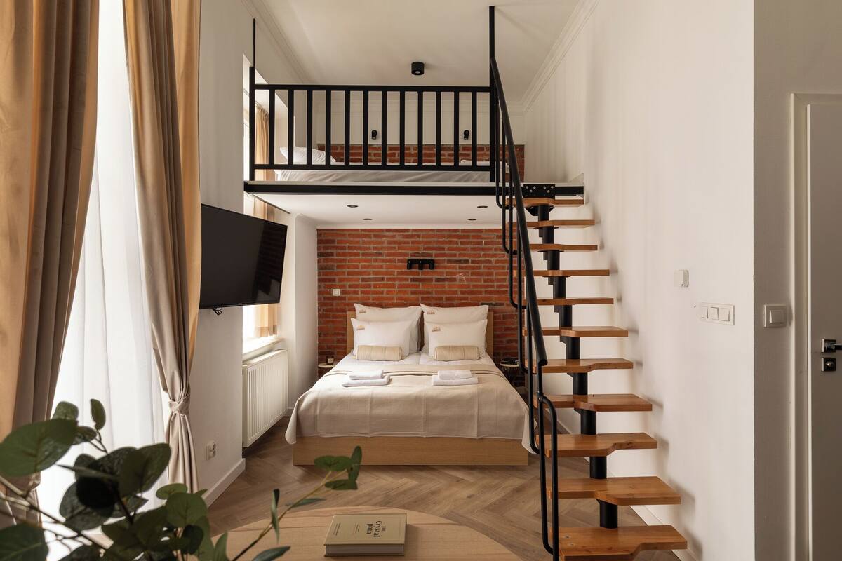 Un dormitorio con cama alta, escalera de madera y pared de ladrillo.